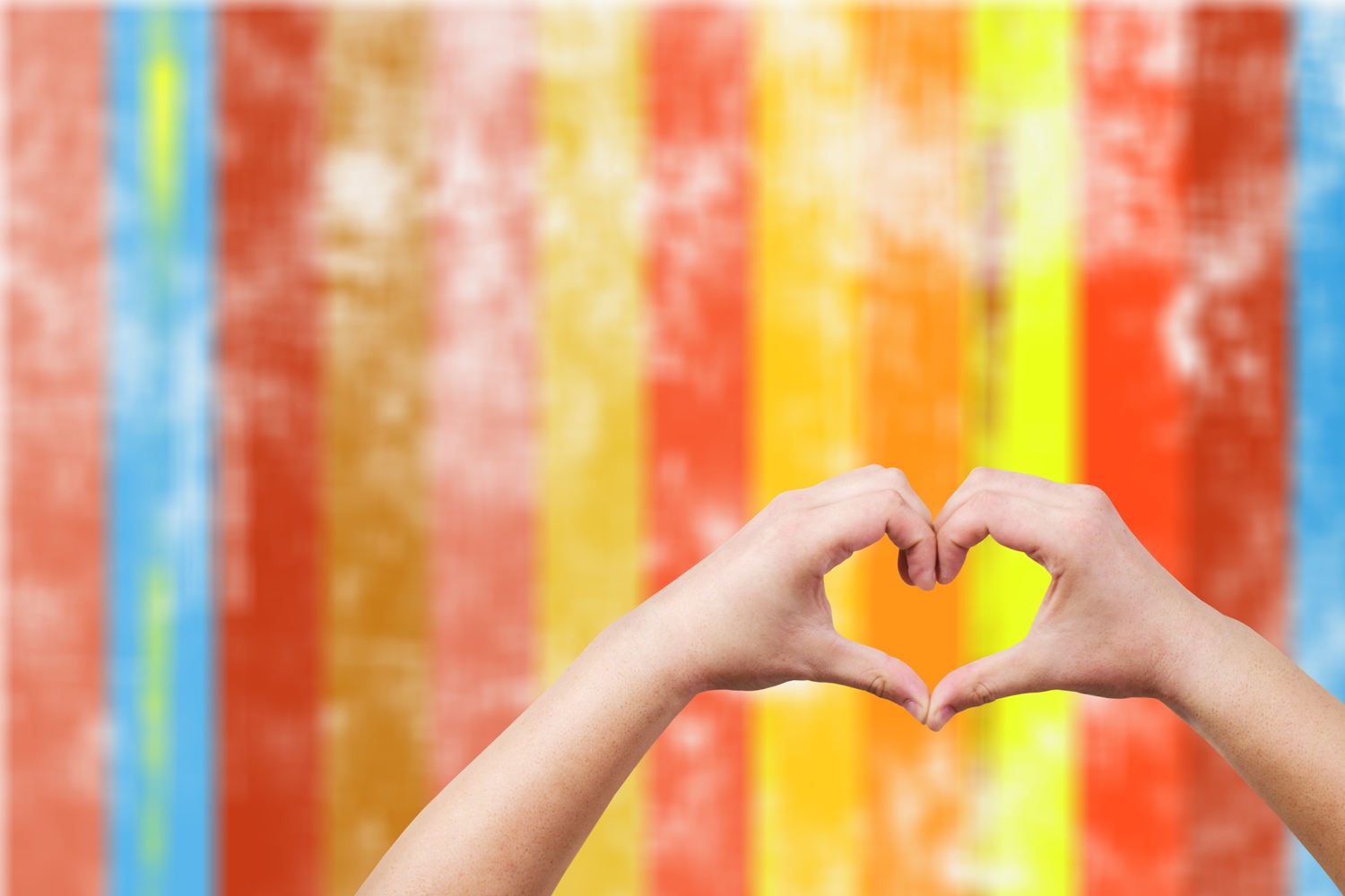 a set of hands making a heart shape with a colorful background